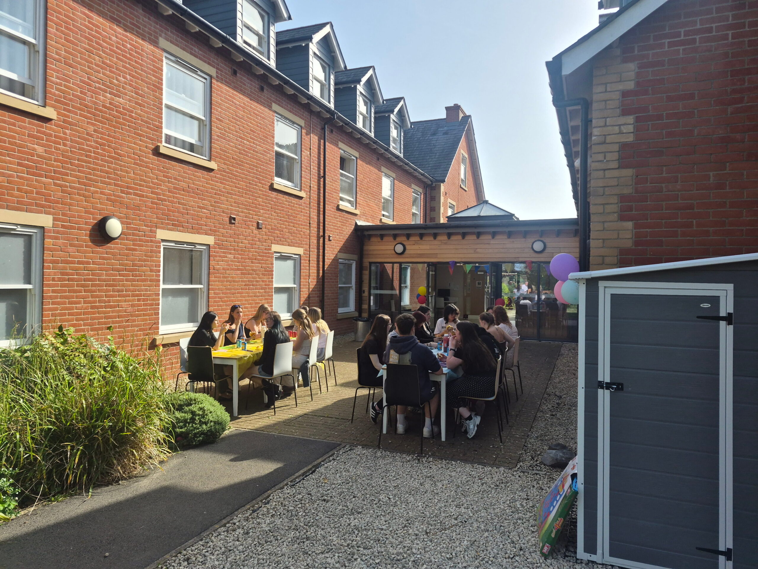 Students eating bbq food at long tables in oak house garden