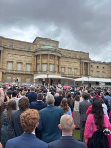 A crowd standing in Buckingham Palace Garden looking up at the Palace.