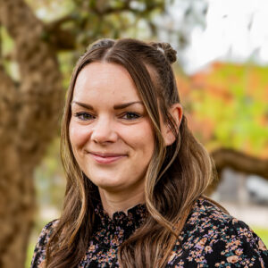 The head and shoulders of a woman with long brown hair. She is wearing a floral top.