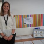 A woman smiles next to a table with EAL content on it.