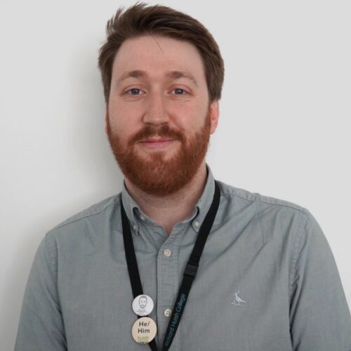 A man with a ginger beard wears a shirt and a lanyard. He is smiling.