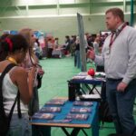 A university or business representative chatting to students at an exhibition stand.