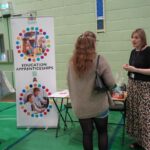 A university or business representative chatting to students at an exhibition stand.