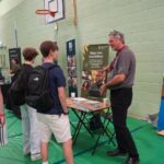 A university or business representative chatting to students at an exhibition stand.
