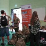 A university or business representative chatting to students at an exhibition stand.