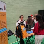 A university or business representative chatting to students at an exhibition stand.