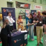 A university or business representative chatting to students at an exhibition stand.