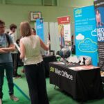 A university or business representative chatting to students at an exhibition stand.