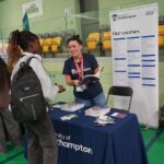 A university or business representative chatting to students at an exhibition stand.