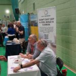 A university or business representative chatting to students at an exhibition stand.