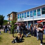 A large group of people on a grassy area. It's sunny.