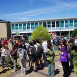 A large group of people on a grassy area. It's sunny.