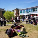 A busy grassy area outside with lots of students milling about chatting.