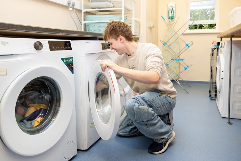 A boy putting clothing into a washing machine in a utility room.
