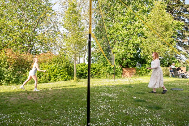 2 students playing badminton in a leafy garden.