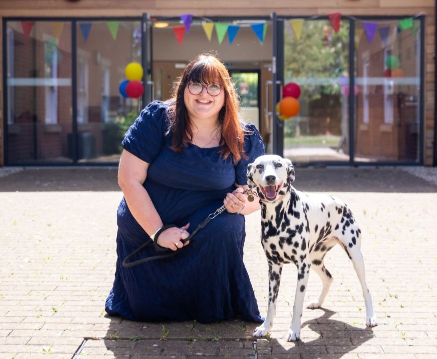 Member of the Oak House team crouching with a Dalmatian dog in the courtyard outside the boarding accommodation, with colourful decorations visible in the background.